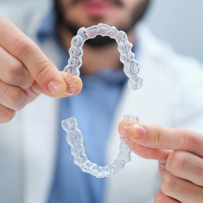 Unrecognizable young orthodontist holding trainer dental braces.